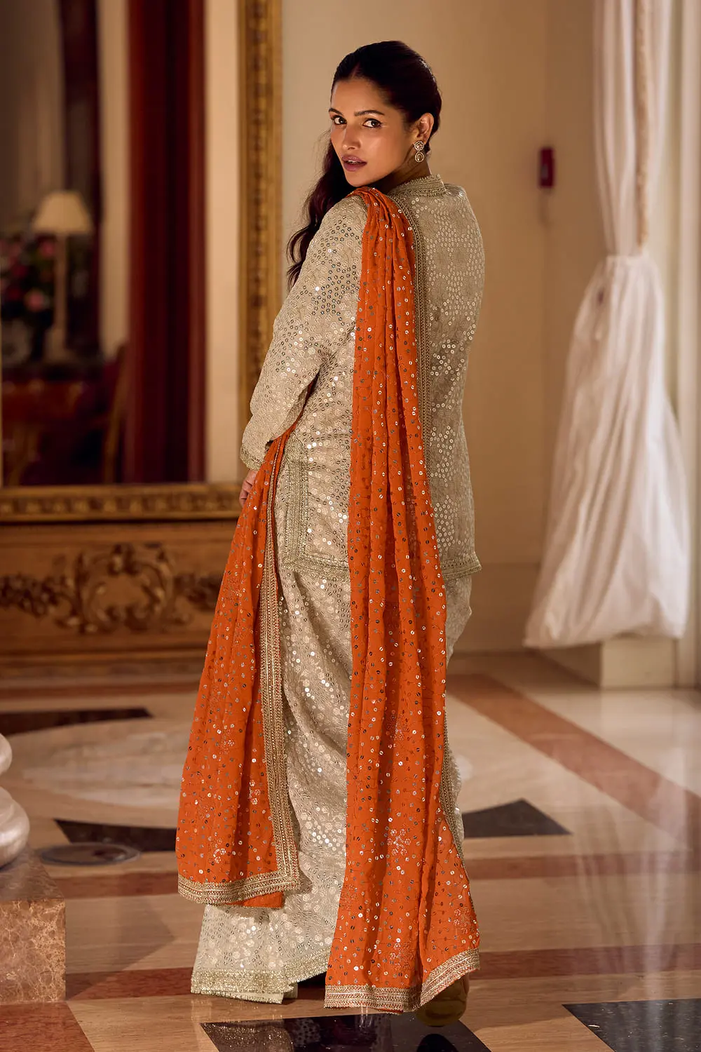 Back profile of the beige dhoti pant and heavy embroidered orange dupatta drape.