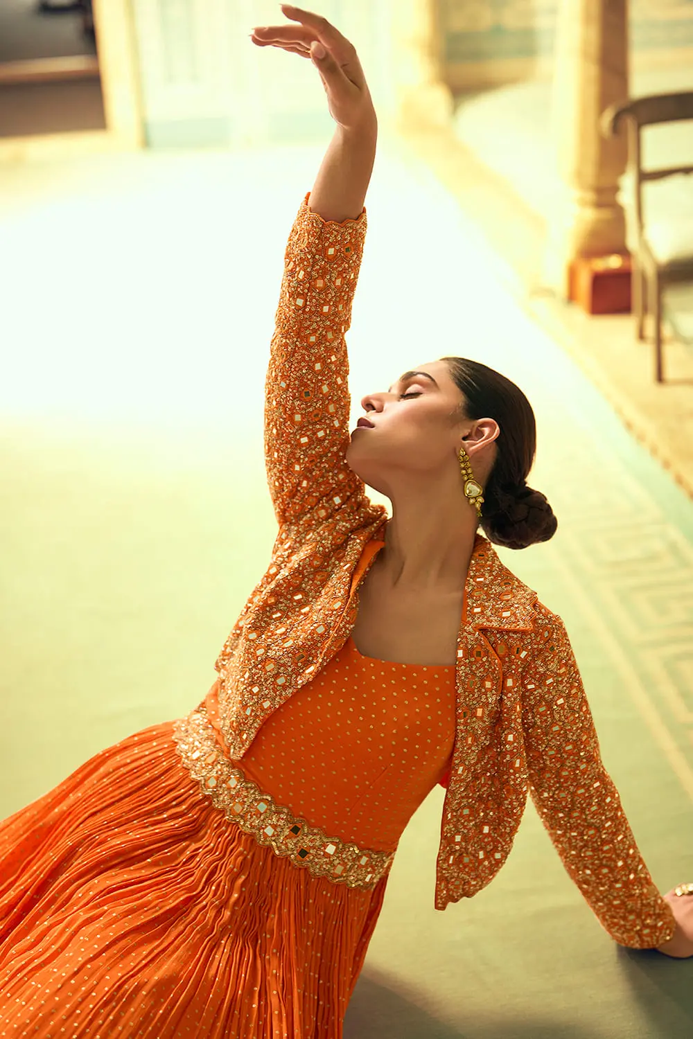 Beautiful sitting pose highlighting the elegant, flowing drape of the orange indowestern anarkali dress with jacket.
